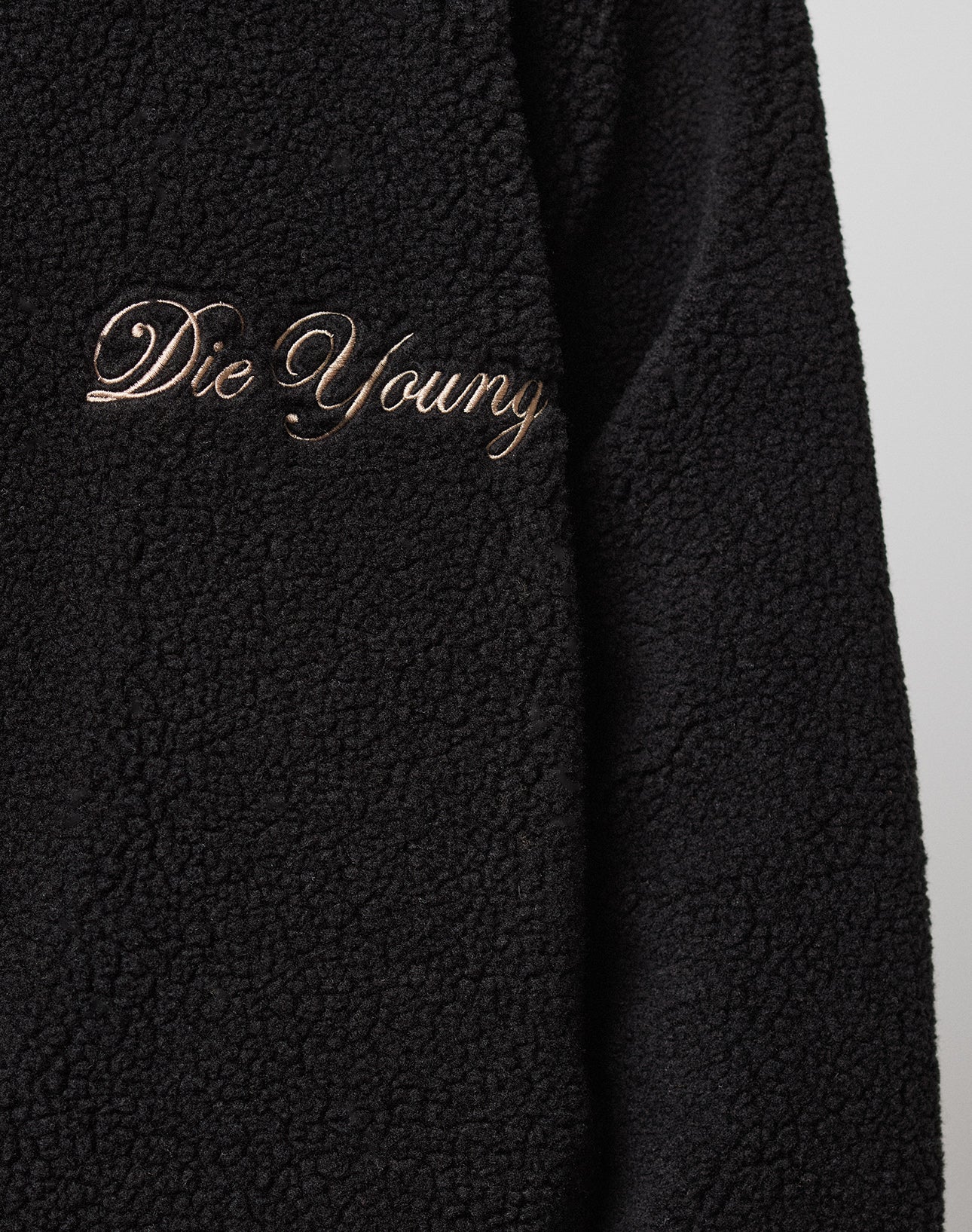 A close-up of the black LFDY Teddy Jacket by LIVE FAST DIE YOUNG, featuring raglan sleeves and "Die Young" embroidered in gold cursive on the chest.