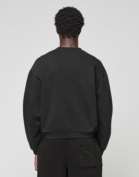 A person with short curly hair, seen from behind, wears the LIVE FAST DIE YOUNG Basic +49 Chest Sweater in black and black pants with a back pocket, standing against a plain light gray background.