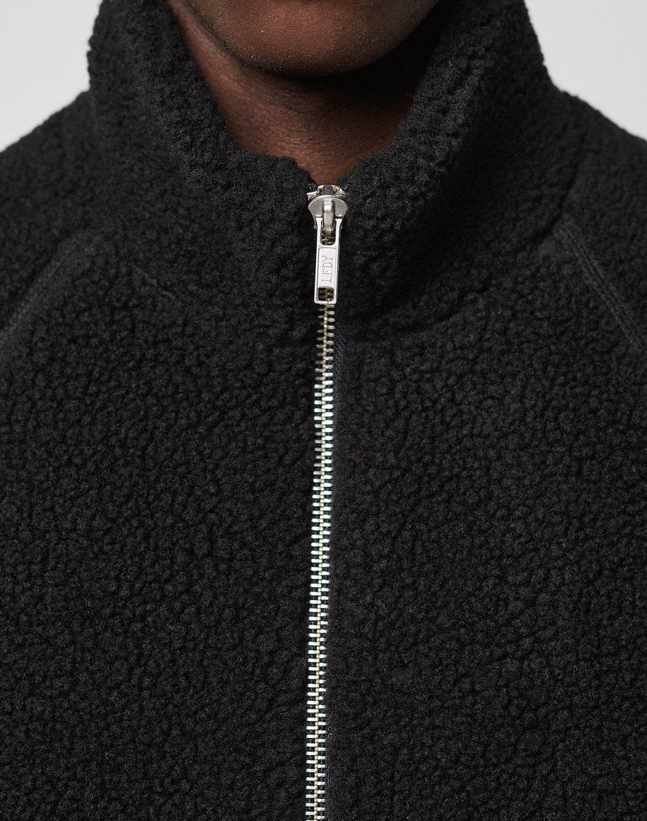 Close-up of a person wearing the LFDY Teddy Jacket by LIVE FAST DIE YOUNG, featuring raglan sleeves and a silver zipper pulled up to the collar; only the lower half of the face and upper chest are visible.
