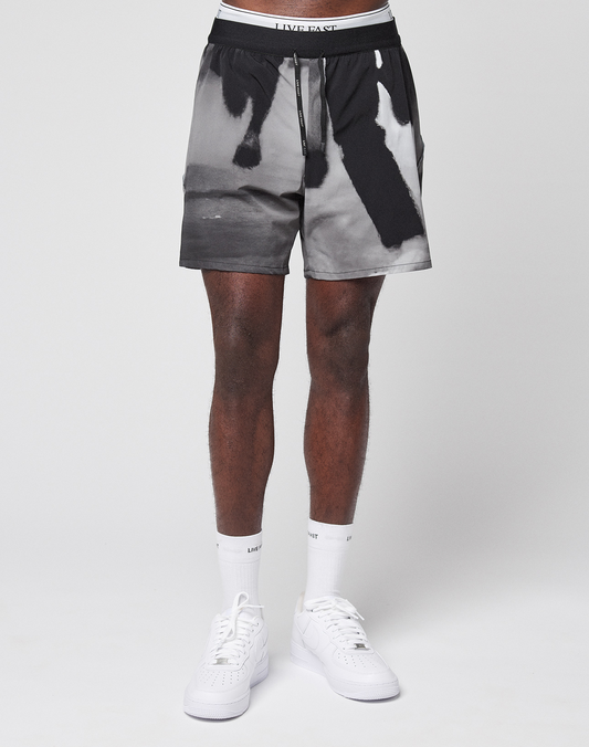 A person wears LIVE FAST DIE YOUNG LFDY Performance Shorts with a black and white graphic design and reflective logo print, paired with white socks and sneakers. Only the lower half is visible against a plain white background.