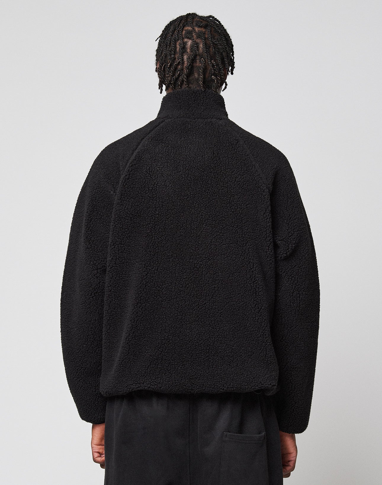 A person with short, twisted hair is seen from behind wearing a black LFDY Teddy Jacket by LIVE FAST DIE YOUNG and black pants, standing against a plain light gray background.