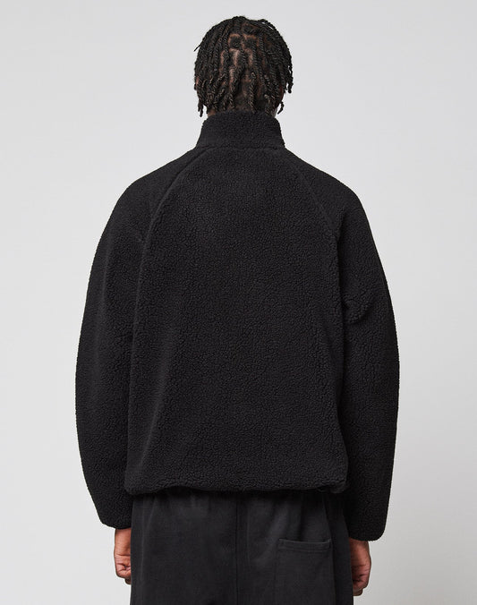 A person with short, twisted hair is seen from behind wearing a black LFDY Teddy Jacket by LIVE FAST DIE YOUNG and black pants, standing against a plain light gray background.