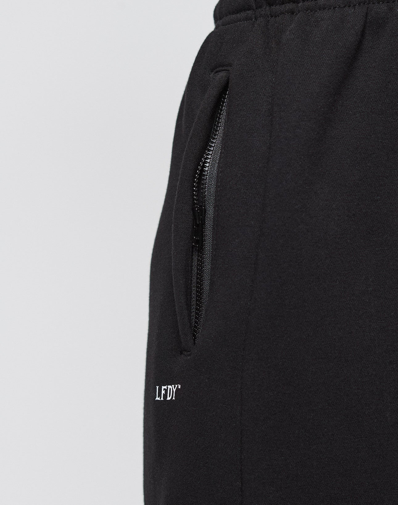 Close-up of the Basic Loose Jogger by LIVE FAST DIE YOUNG: black athletic pants in a loose fit with elastic waistband, a zippered side pocket, and a small white LFDY logo embroidered near the left pocket.