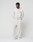 A man stands against a white background wearing LIVE FAST DIE YOUNG's off-white Heavyweight Loungepants and matching 650gsm hoodie with a red chest graphic, paired with white sneakers. His hands are in his pockets as he looks to the side.