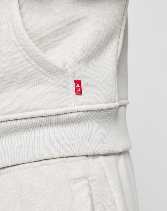 Close-up of a person in the LFDY Heavyweight Lounge Zip Hooded by LIVE FAST DIE YOUNG and matching sweatpants, featuring a small red tag with white text on the side seam near the waist.
