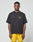 A man faces forward against a plain light gray background, wearing the LIVE FAST DIE YOUNG LFDY Circle Dog Tee in loose oversize fit with a small yellow graphic, paired with yellow shorts.