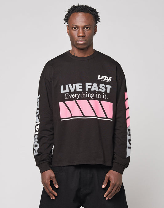 A man wears the LFDY Racing Longsleeve by LIVE FAST DIE YOUNG—an oversized black shirt with “LIVE FAST Everything in it.”, pink stripes, bold white sleeve text, 100% Baumwolle, and reflektierendem Print—set against a plain light background.