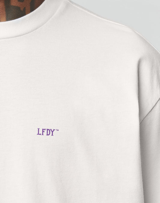 Close-up of a person wearing the LFDY Originals Tee by LIVE FAST DIE YOUNG, featuring small purple LFDY™ embroidery on the upper chest. The image shows part of the neck and shoulder, highlighting its clean oversized fit.