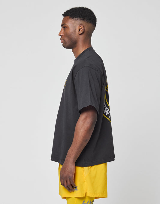 A man in profile against a plain background wears the LIVE FAST DIE YOUNG LFDY Circle Dog Tee, an oversized black 100% Baumwolle shirt featuring a back graphic, paired with bright yellow shorts.
