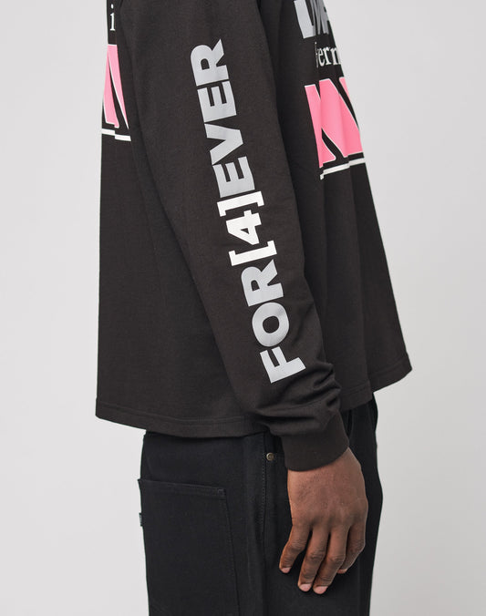 Someone wearing the LFDY Racing Longsleeve by LIVE FAST DIE YOUNG—black, oversize fit with FOR[4]EVER in large white sleeve letters and pink/white chest graphics, made from 100% Baumwolle. Only their torso and one arm are visible.