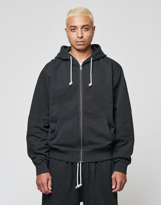 A person with short blond hair wears a black LIVE FAST DIE YOUNG LFDY Lightweight Hooded Zip and matching black pants, standing facing the camera against a plain light background.