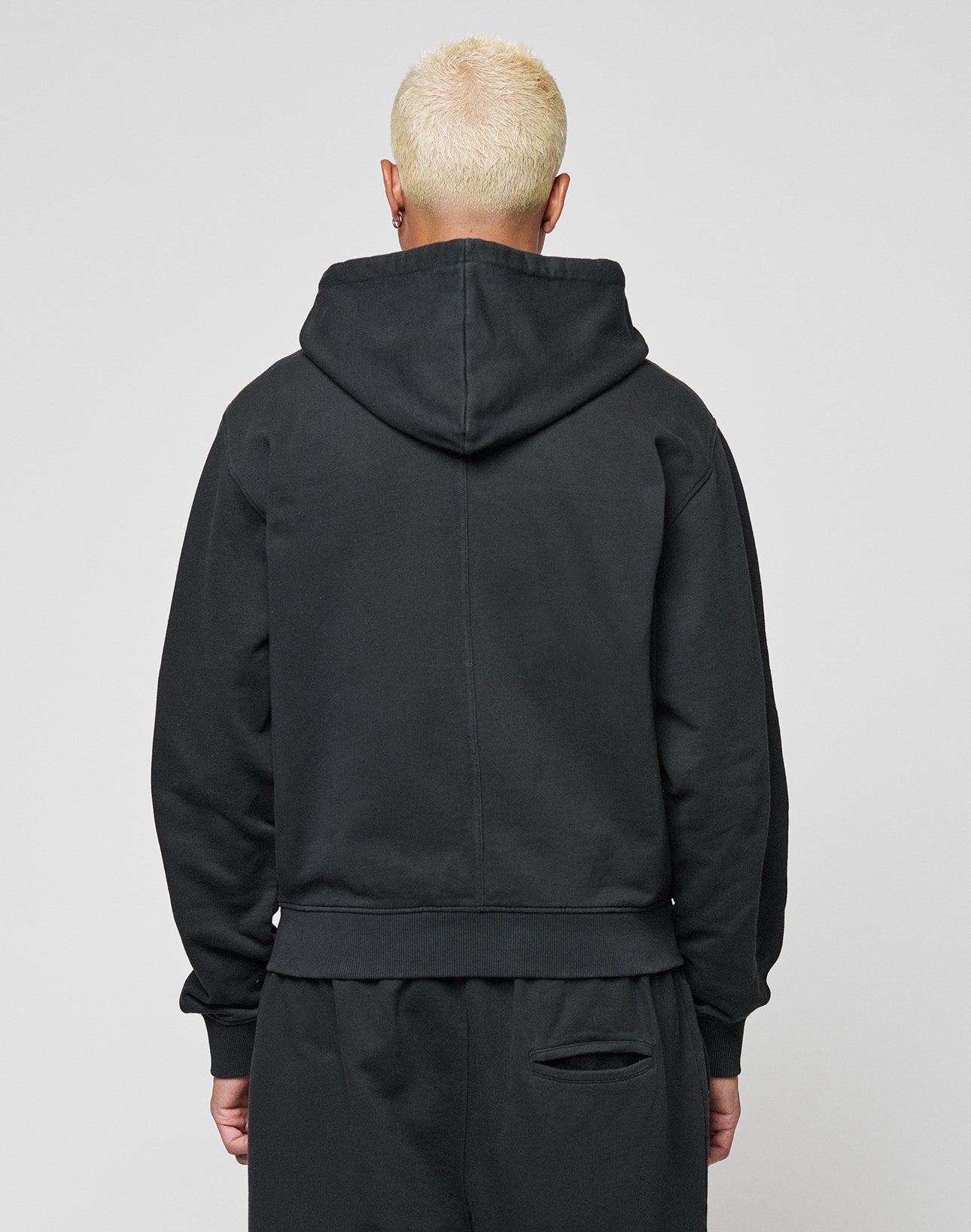 A person with short, bleached blond hair is seen from behind in a LIVE FAST DIE YOUNG LFDY Lightweight Hooded Zip and matching black pants, hood down, against a plain gray background.
