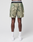 A person stands facing away, wearing green and beige LFDY Performance Running Shorts by LIVE FAST DIE YOUNG with built-in tights, white socks, and white sneakers against a plain light gray background.