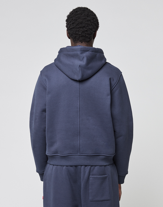 A person with short curly hair is seen from behind, wearing the LIVE FAST DIE YOUNG LFDY Heavyweight Lounge Hooded in navy blue with matching pants featuring a back pocket, against a plain light background. Made from 100% Baumwolle.