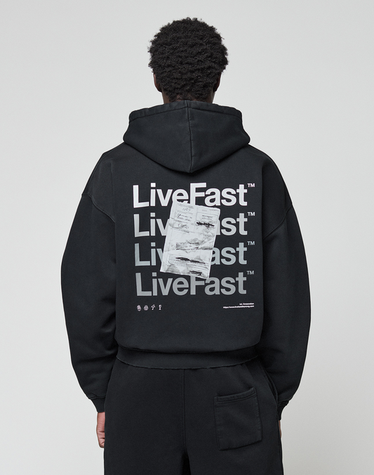 A person wearing the LIVE FAST DIE YOUNG Basic Evidence Hooded Zip in an oversize fit, featuring bold white branding, paper-like graphic, small symbols, and subtle distressing on the back, stands against a plain background. | model