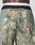 Close-up of the back of a person wearing green and tan camouflage LFDY Performance Running Shorts by LIVE FAST DIE YOUNG, featuring a black waistband, white elastic band, and reflective LIVEFAST logo print.