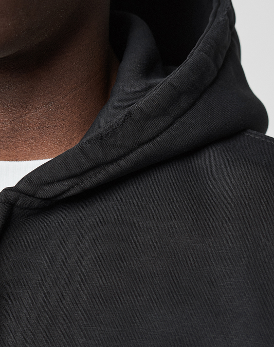Close-up of a person wearing the LIVE FAST DIE YOUNG Basic Evidence Hooded Zip in black over a white shirt; only part of the face, neck, and shoulder are shown, highlighting the fabric, seam details, and subtle brand logo on the hoodie.