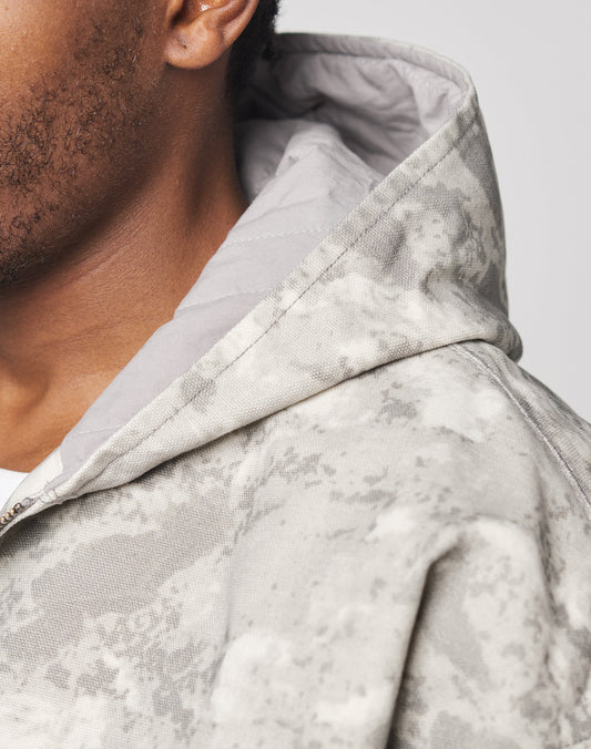 Close-up of a person wearing the LIVE FAST DIE YOUNG Live Fast Canvas Jacket in a light gray and white camouflage Oversize Fit; only part of their face, ear, and shoulder are visible.