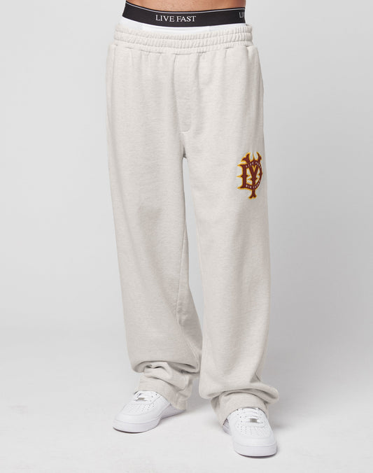 A person wears LIVE FAST DIE YOUNG’s DY Jogger in an oversize fit with a gold and red emblem on the left thigh, wide leg style, a black LIVE FAST waistband, white sneakers, and a plain white background.