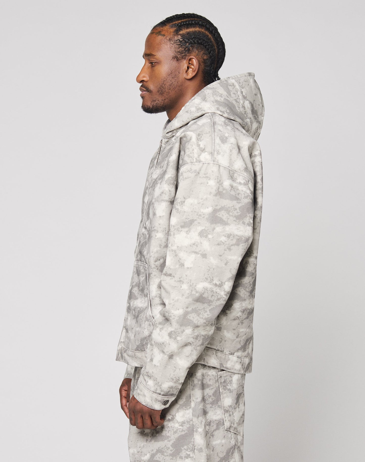 A man with braided hair stands in profile against a plain white background, wearing an oversize fit Live Fast Canvas Jacket by LIVE FAST DIE YOUNG.