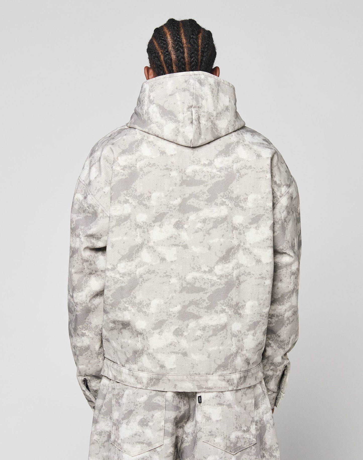 A person with braided hair is seen from behind, wearing the LIVE FAST DIE YOUNG Live Fast Canvas Jacket and matching pants in a light gray camouflage pattern against a plain background.