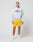 A person stands against a plain background wearing a gray Live Fast Beware Hooded by LIVE FAST DIE YOUNG, featuring a front print, paired with yellow shorts, white socks, and white sneakers.