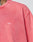 Close-up of a person wearing the LIVE FAST DIE YOUNG Basic Evidence Tee, an oversized faded pink shirt made from 100% Baumwolle, featuring small white LFDY™ text on the chest. Part of their neck, a tattoo, and the Flag-Label are visible.