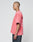 A person with a shaved head in profile wears the LIVE FAST DIE YOUNG Basic Evidence Tee—an oversize, faded pink shirt with a Flag-Label and black and white back text—paired with dark pants against a plain light background.