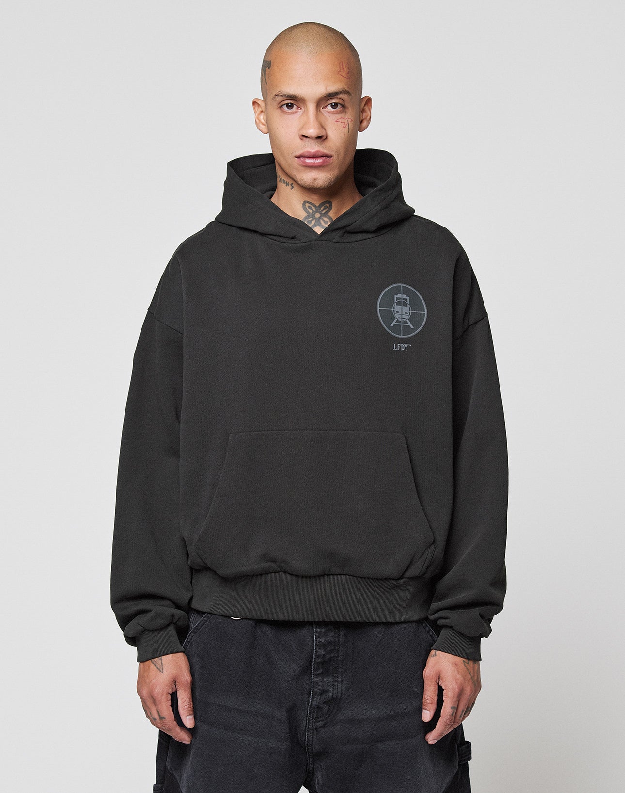 A person with a shaved head wears the LFDY Vandals Hooded by LIVE FAST DIE YOUNG, made from 100% cotton, paired with black pants. The oversize hoodie features a double-layered hood and a small logo on the left chest, set against a white background.