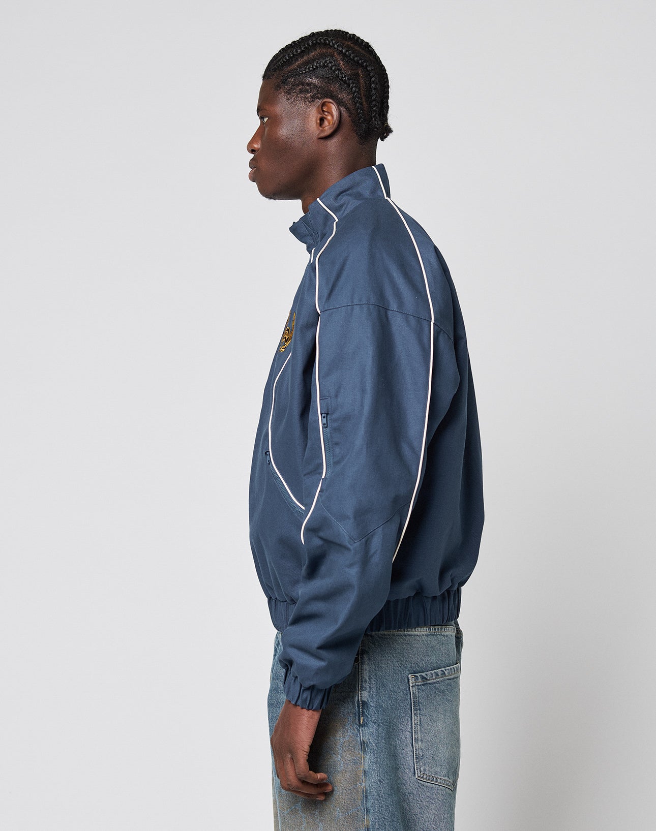 A person with braided hair wears the LFDY Canvas Jacket by LIVE FAST DIE YOUNG and light blue jeans, standing in profile against a plain light gray background.