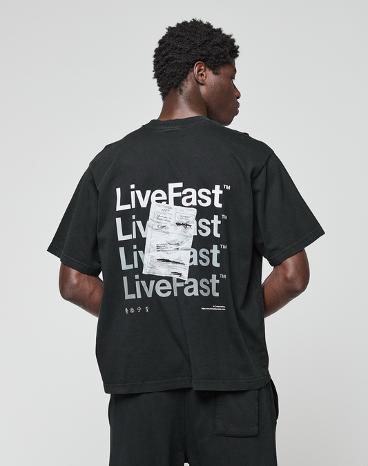 A person faces away from the camera wearing the LIVE FAST DIE YOUNG Basic Evidence Tee, an oversized black T-shirt with “LiveFast” repeatedly printed in white on the back and a visible white tag attached.