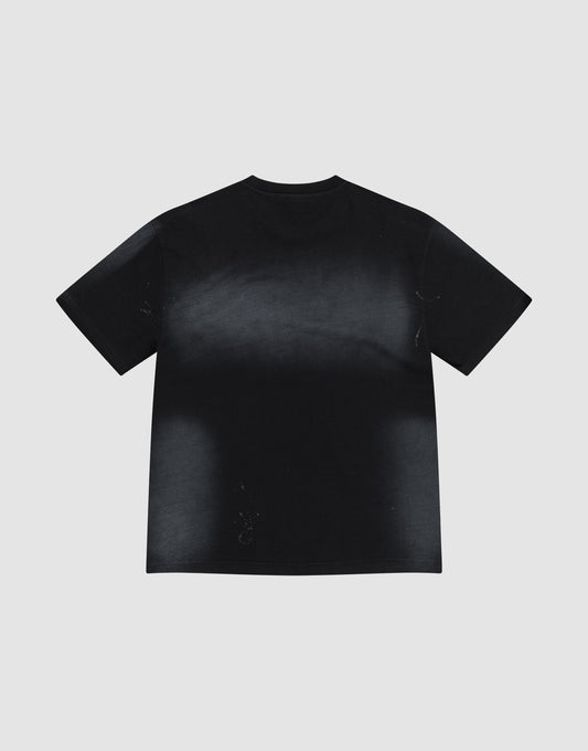 The Live Fast Rivet Tee by LIVE FAST DIE YOUNG is a black, oversized short-sleeve t-shirt with a faded, slightly distressed look and hand-applied spray effect, made from 100% cotton. Pictured flat on a light gray background with its back visible.