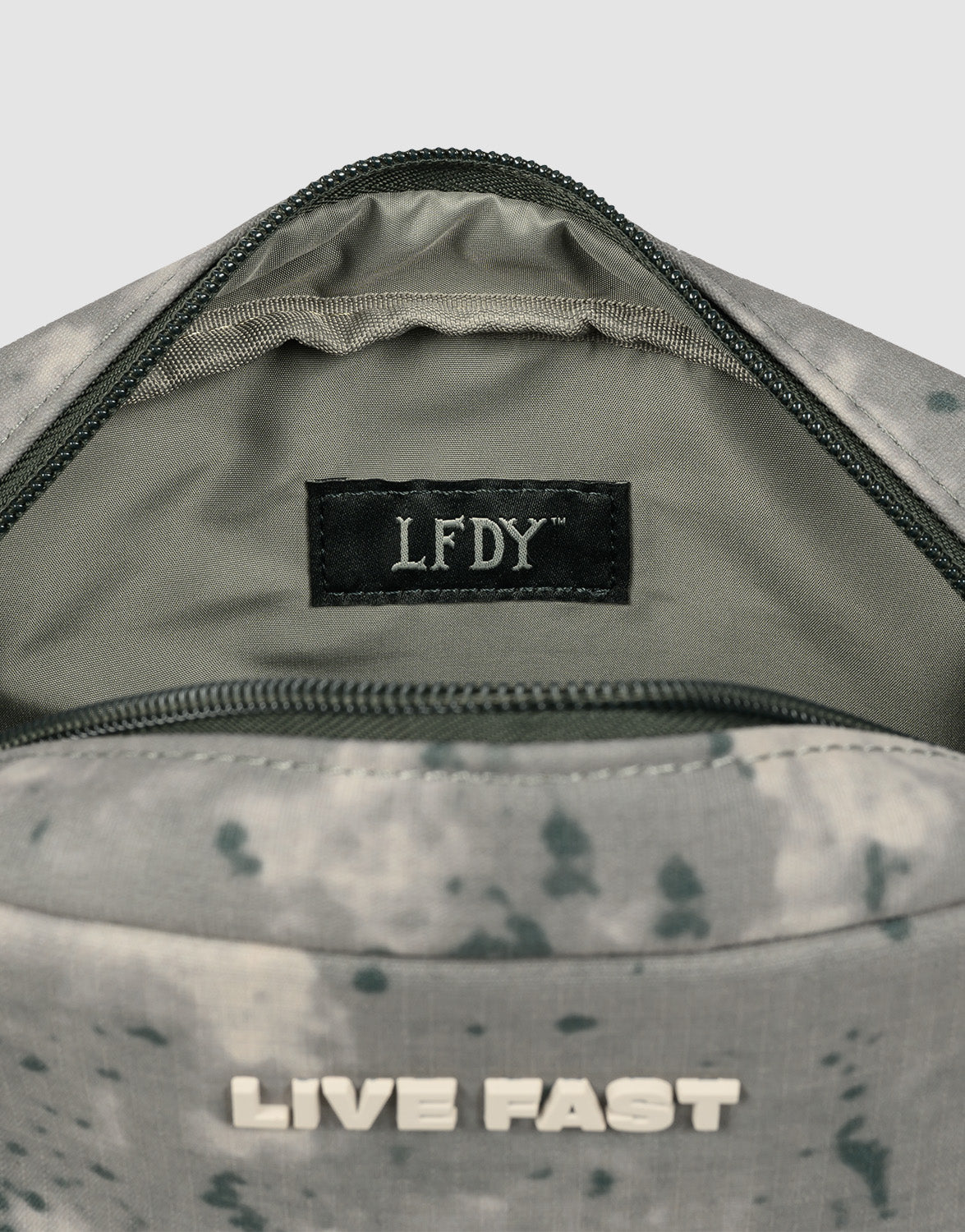 Close-up of the LFDY Amenity Kit by LIVE FAST DIE YOUNG: an open gray patterned bag with a side handle, large visible zippered pocket, black LFDY label inside, "LIVE FAST" in white on the outside. Made from 100% polyester.