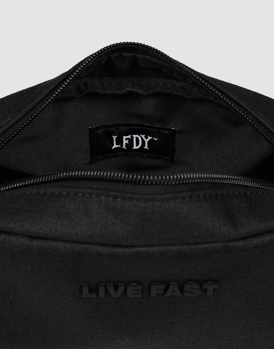 A close-up of the LFDY Amenity Kit by LIVE FAST DIE YOUNG—a black polyester zippered bag with "LIVE FAST" embossed outside and an LFDY label inside, partially open to show its inner pockets and large zip compartment.