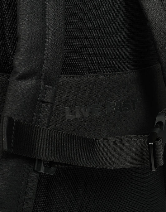 Close-up of the black LFDY Backpack (19L) by LIVE FAST DIE YOUNG, with "LIVE FAST" subtly printed on the fabric, partially covered by a strap and plastic buckle, and featuring adjustable shoulder straps for comfort.