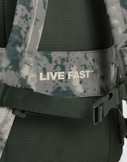 Close-up of the LFDY Backpack by LIVE FAST DIE YOUNG: a green and gray camo 19L laptop rucksack with mesh back, adjustable shoulder straps, and "LIVE FAST™" printed in white on a horizontal strap.