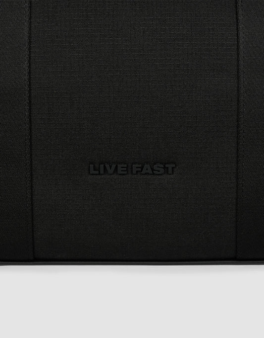 A close-up of black textured polyester from the LFDY Utility Bag by LIVE FAST DIE YOUNG, featuring "LIVE FAST" embossed in the center and hinting at its großes Fach for practical use.