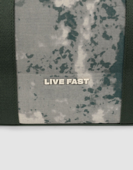 A close-up of the LFDY Utility Bag by LIVE FAST DIE YOUNG shows camouflage fabric with LIVE FAST in bold white letters and sturdy Tragegurte for easy carrying.