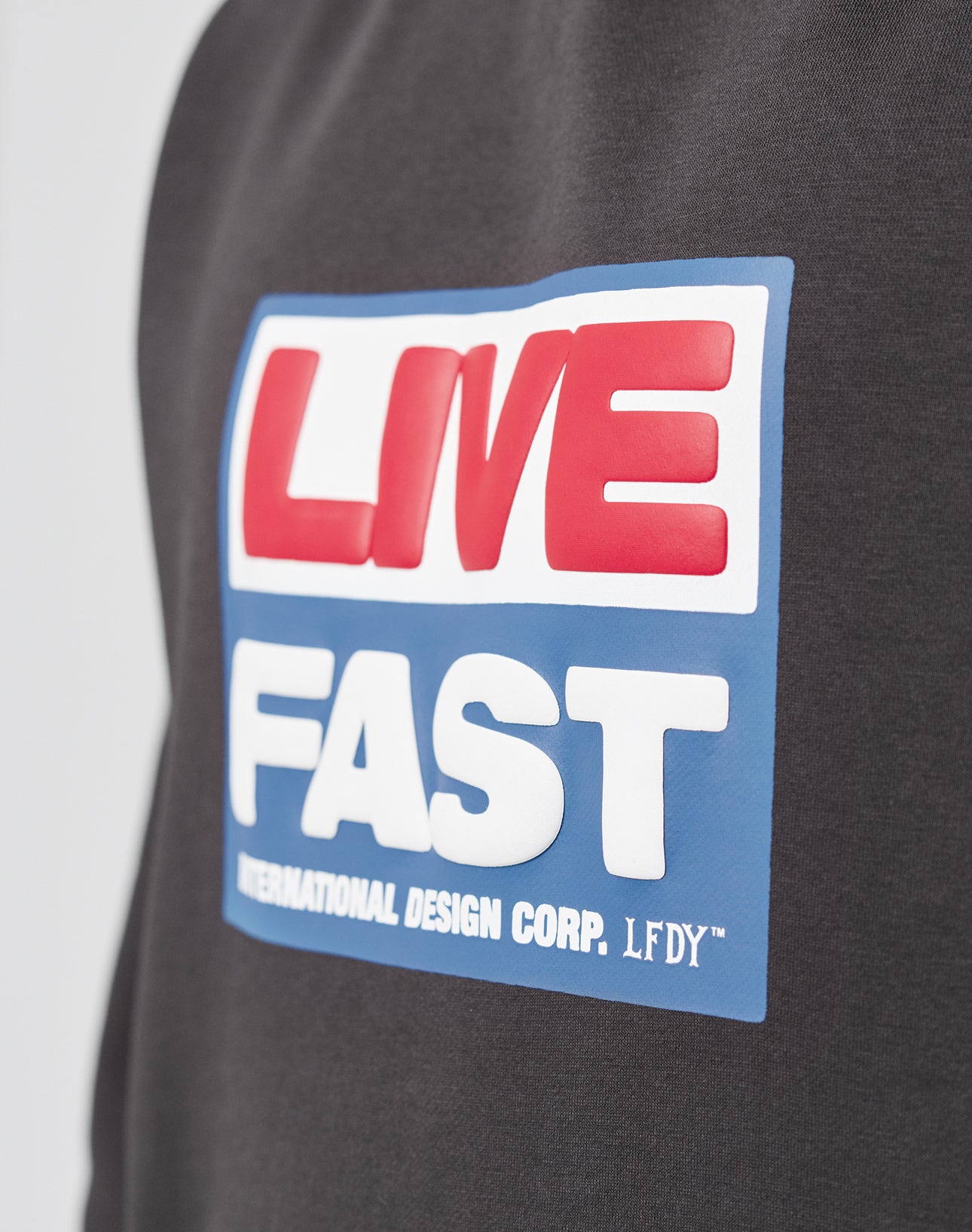 Close-up of the LIVE FAST DIE YOUNG Live Fast Box Hooded sweatshirt, oversized fit, featuring a puffer print reading LIVE in red on white and FAST in white on blue, with INTERNATIONAL DESIGN CORP. LFDY™ below.