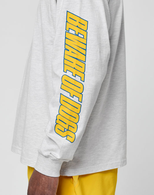 Someone wearing the LFDY Split Sphere Longsleeve by LIVE FAST DIE YOUNG in light gray with bold yellow and blue BEWARE OF DOGS sleeve print, paired with bright yellow shorts. Made from pure cotton and includes practical care instructions.