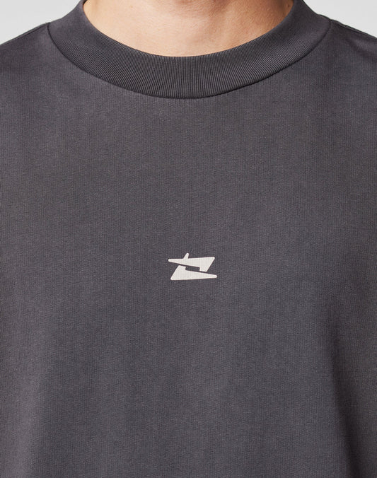 Close-up of someone wearing the LIVE FAST DIE YOUNG Live Fast Cropped Oversized Tee in dark gray, featuring a small white geometric “Z” logo at the center chest.