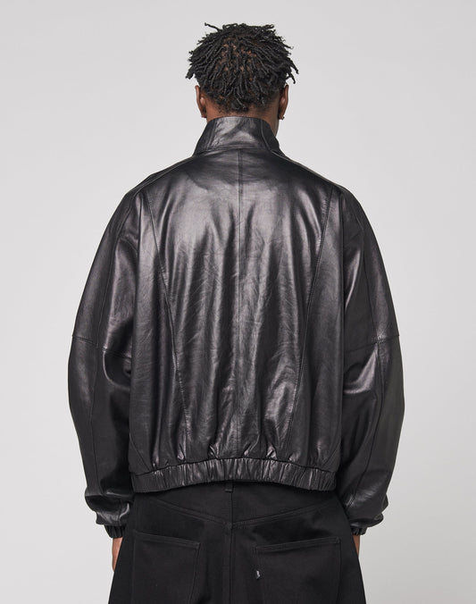 A person with short, twisted hair is shown from behind wearing the LIVE FAST DIE YOUNG Live Fast Leather Trackjacket with Stehkragen and black pants, standing against a plain light gray background.