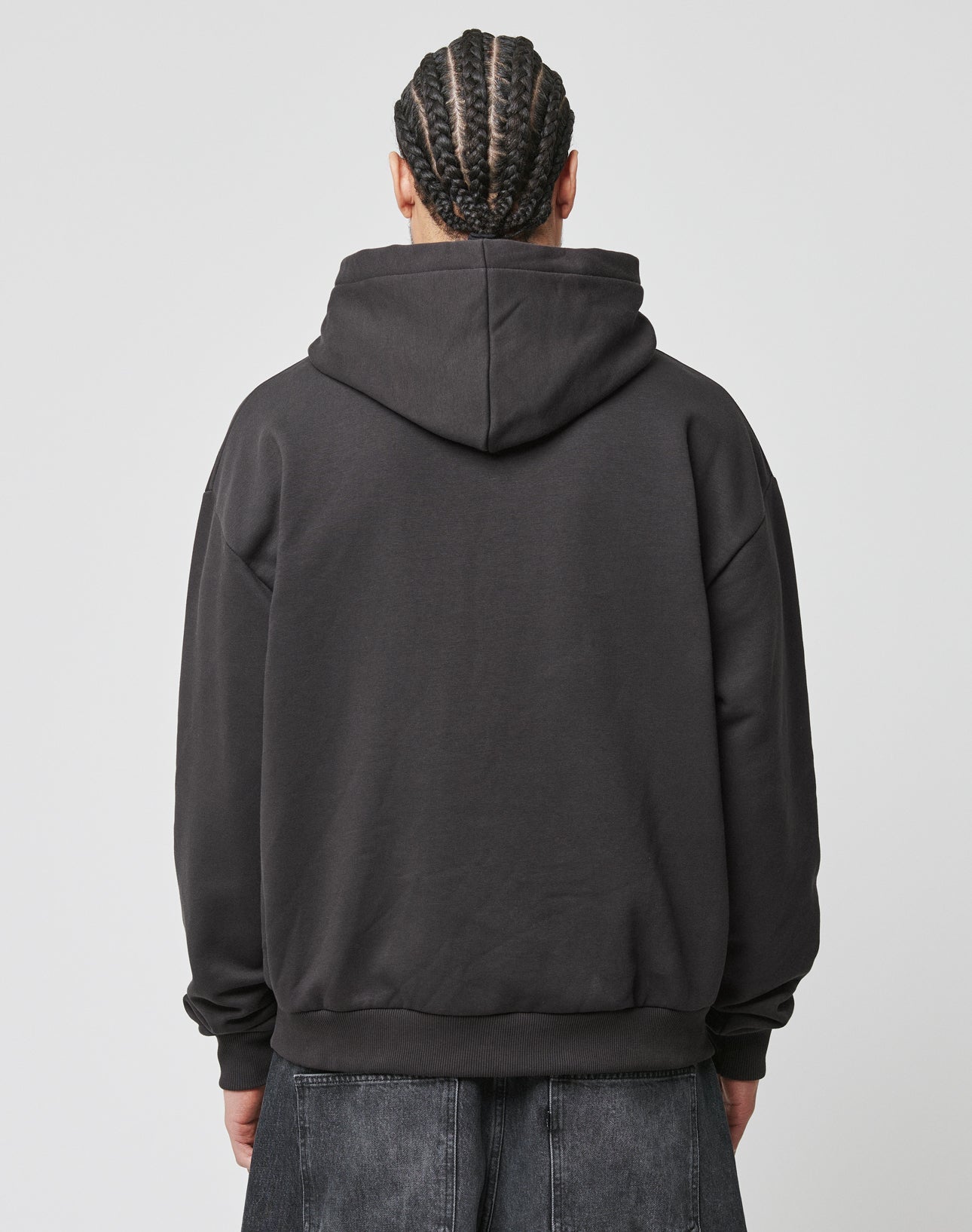 A person with braided hair, seen from behind, wears the LIVE FAST DIE YOUNG Live Fast Box Hooded black puffer print sweatshirt (oversized fit) and dark pants against a plain light background.