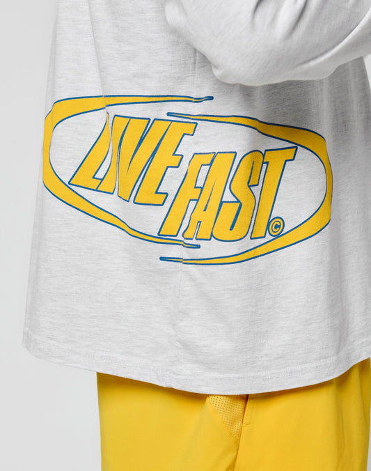 Someone wears the LFDY Split Sphere Longsleeve by LIVE FAST DIE YOUNG, an oversize fit light gray shirt with bold yellow and blue LIVE FAST text, paired with bright yellow pants—crafted from weicher Baumwolle for comfort and easy-care Pflege.