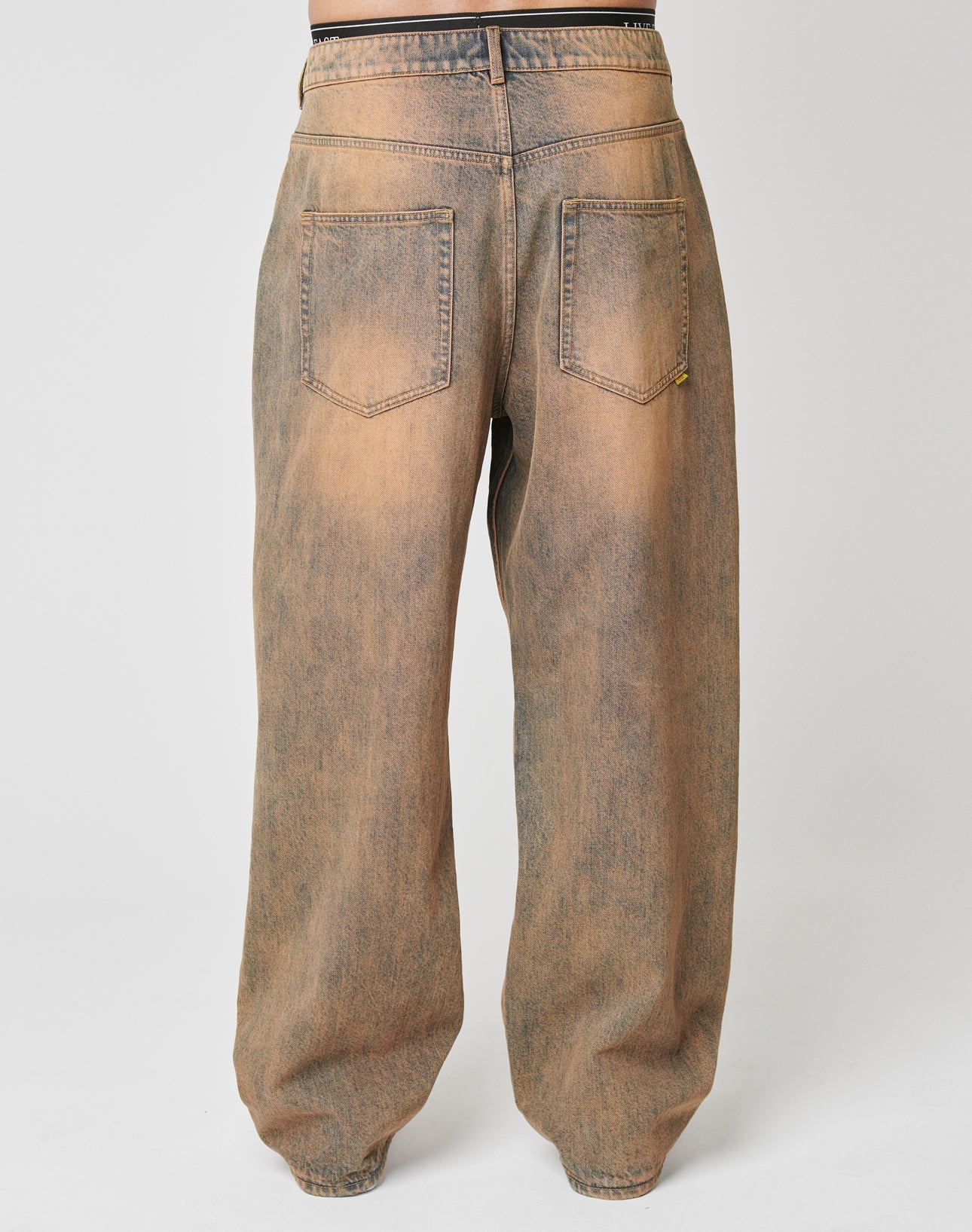 Back view of a person in LIVE FAST DIE YOUNGs LFDY Baggy Denim—brownish-black faded, 100% Baumwolle jeans with two back pockets, a vintage look, and weites gerades Bein that pools at the ankles for relaxed style.