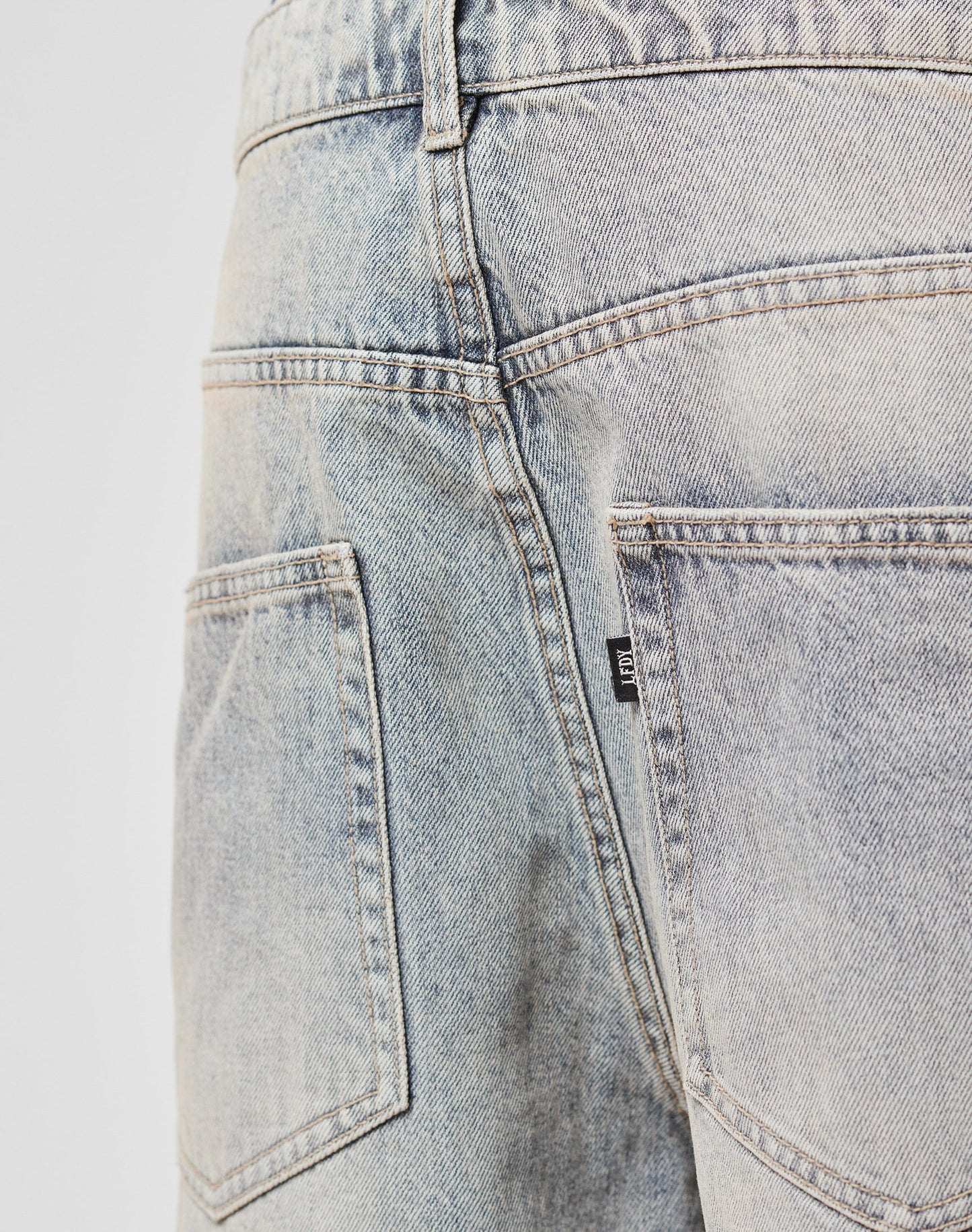Close-up of the back of LFDY Baggy Denim, featuring a light-wash finish, baggy fit, two back pockets, faded fabric details, visible stitching, and a small black and white flag label on the seam near the right pocket.