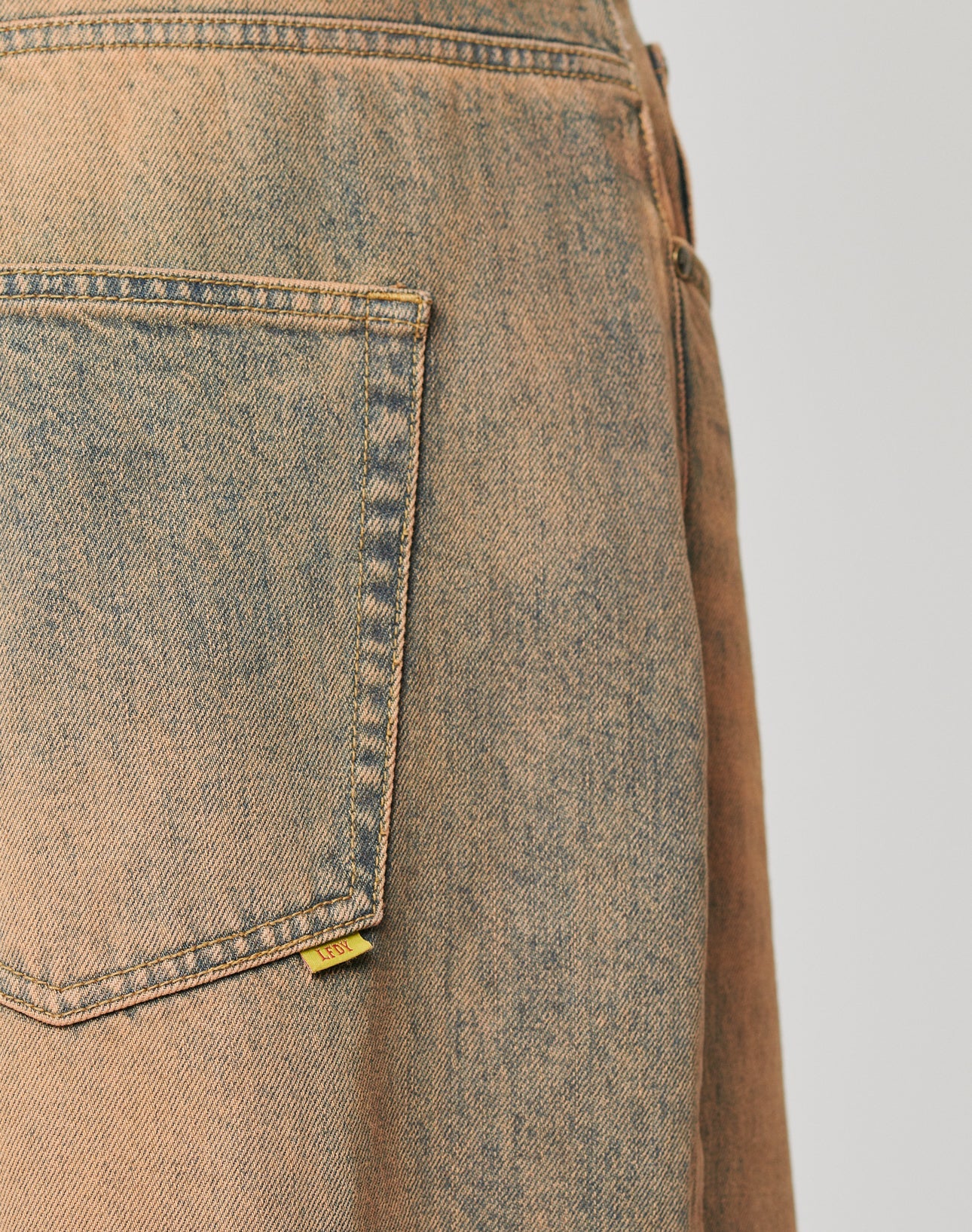 Close-up of the back pocket on LIVE FAST DIE YOUNGs LFDY Baggy Denim, faded light brown jeans with a yellow tag. Made from 100% Baumwolle, these jeans offer a comfortable Baggy Fit for relaxed everyday style.