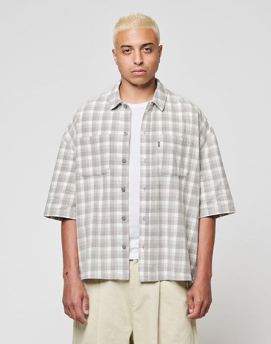 A person with short bleached blonde hair wears the LFDY Light Flannel by LIVE FAST DIE YOUNG in grey and white vintage wash over a white T-shirt and beige pants, standing against a plain light background. | model