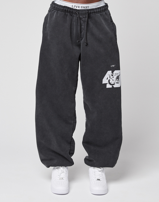 Someone wears the LFDY 40 Wide Cuff Jogger by LIVE FAST DIE YOUNG—oversized dark gray cotton sweatpants with a white tiger and "40" graphic on one leg, side pockets, paired with white sneakers and a visible LIVE FAST waistband.