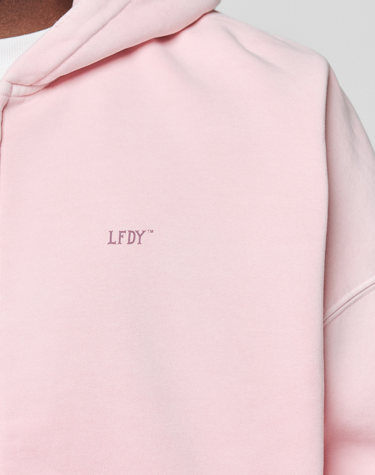 Close-up of a person wearing the light pink Basic Evidence Hooded Zip by LIVE FAST DIE YOUNG, featuring small purple LFDY-Branding embroidered on the chest. The hood and part of the shoulder are visible.